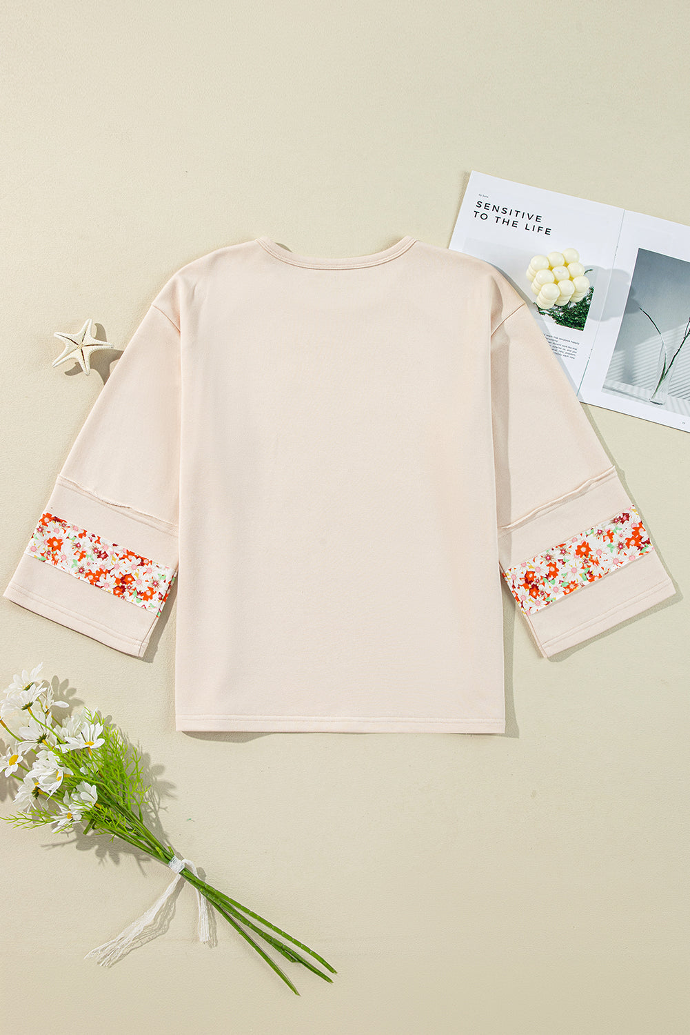 Beiges Oberteil mit Blumen-Patch-Grafik, sichtbaren Nähten und weiten Ärmeln