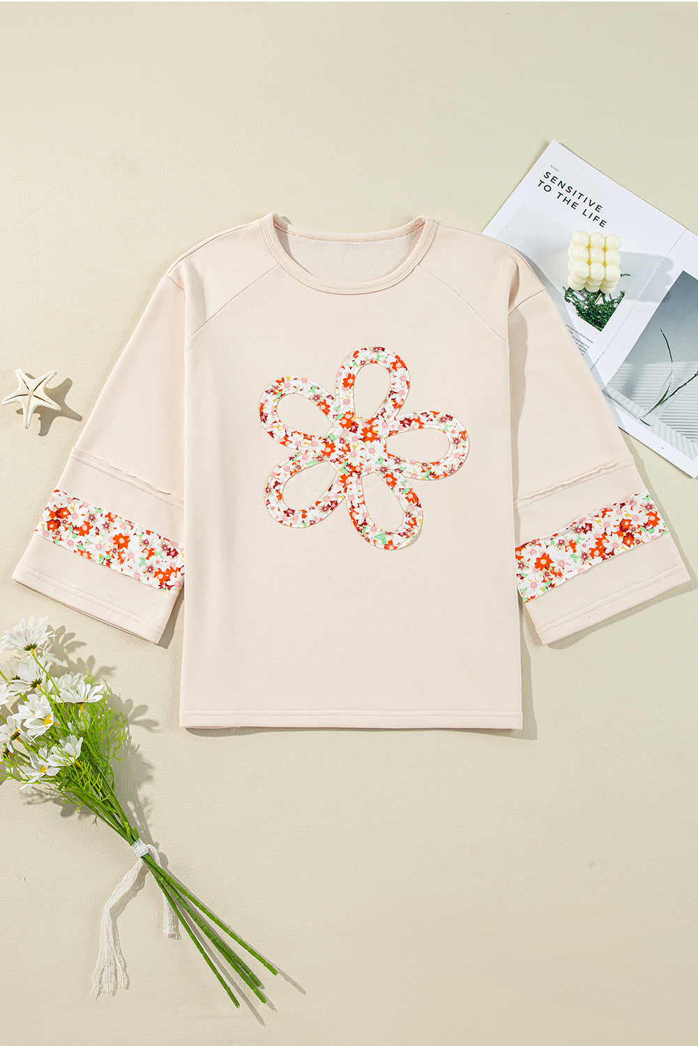 Beiges Oberteil mit Blumen-Patch-Grafik, sichtbaren Nähten und weiten Ärmeln