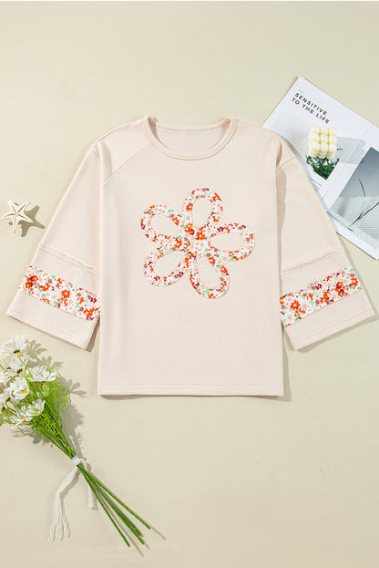 Beiges Oberteil mit Blumen-Patch-Grafik, sichtbaren Nähten und weiten Ärmeln