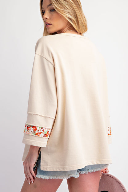 Beiges Oberteil mit Blumen-Patch-Grafik, sichtbaren Nähten und weiten Ärmeln